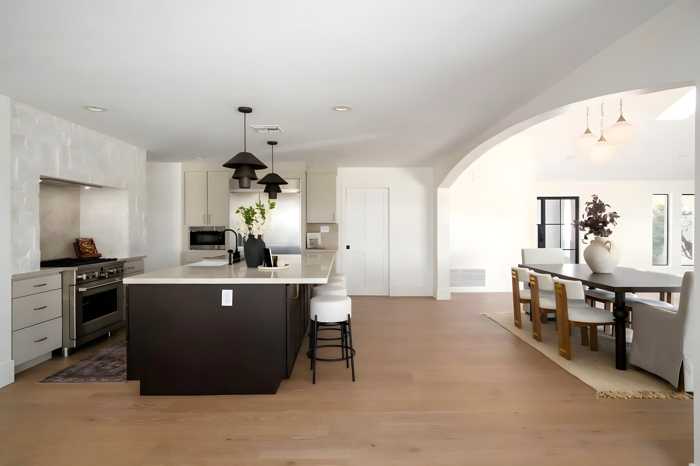 The open floor plan connects the kitchen island to the dining space through matching stone countertops and cohesive lighting design.
