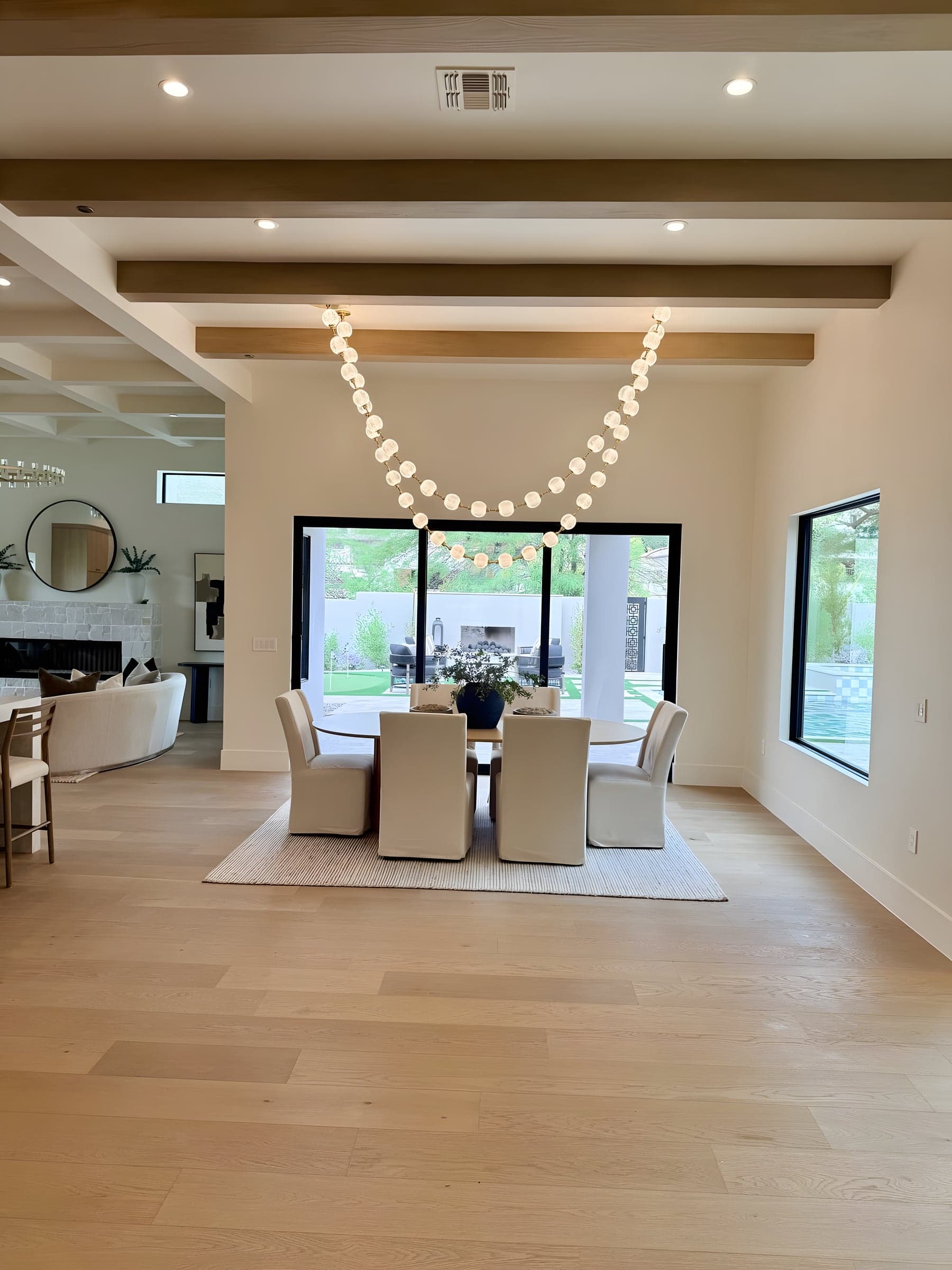 Natural wood beams and a sculptural chandelier set the tone for this dining room, with sliding doors opening directly to the pool terrace.