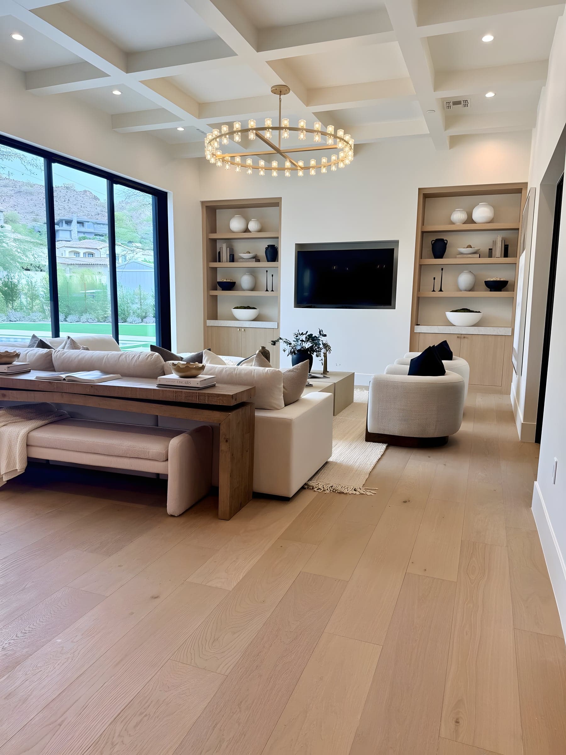 A statement ring chandelier anchors this great room — coffered ceilings and white oak built-ins frame the desert views beyond.