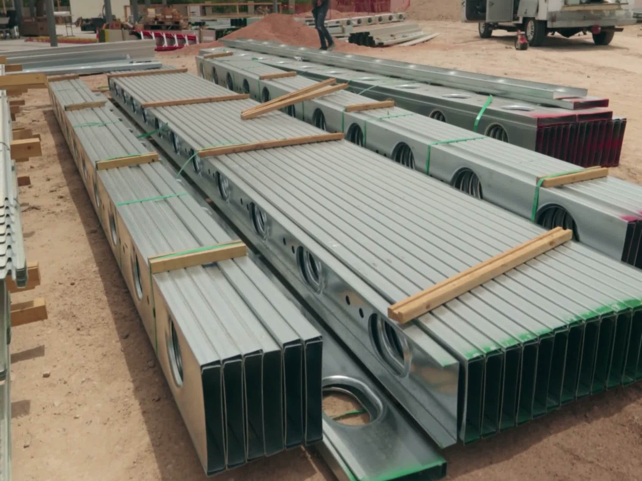 Stacked galvanized structural-phase steel (set by the project's steel trade) members staged on site